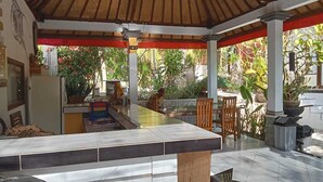A covered outdoor dining area with a tiled floor, wooden chairs, and a central table. - Ratu Cottage by OurStory Travels (Penida Island)