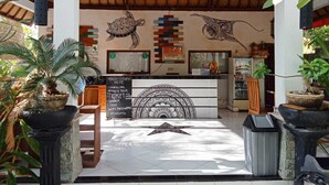 A reception area with a wooden ceiling, a black signboard with text, and decorative wall art. - Ratu Cottage by OurStory Travels (Penida Island)