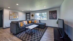 A modern living room with a gray sectional sofa, a white coffee table, and a flat-screen TV. - Cozy Air-conditioned Retreat 3 mins from Airport (SeaTac)