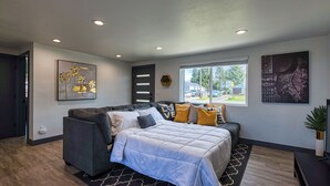 A modern living room with a sofa, a large bed, and artwork on the walls. - Cozy Air-conditioned Retreat 3 mins from Airport (SeaTac)