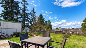 A deck with a table and chairs, surrounded by a grassy yard and trees. - Cozy Air-conditioned Retreat 3 mins from Airport (SeaTac)