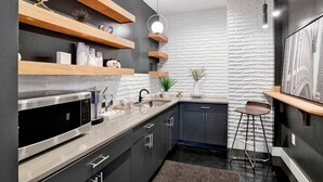 A modern kitchen with wooden shelves, a stainless steel microwave, and a bar area with stools. - Beautiful 1 BR Renovated Apt in downtown (Mobile)