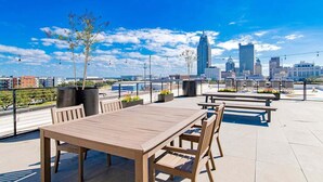 An outdoor patio with wooden tables and chairs, potted plants, and a city skyline in the background. - Beautiful 1 BR Renovated Apt in downtown (Mobile)