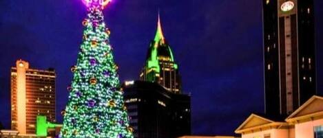 A large Christmas tree with lights and a neon sign at the top, surrounded by buildings and a clock tower.