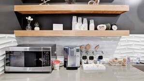 A kitchen with a microwave, coffee maker, and various kitchen items on the counter. There are wooden shelves above the counter holding decorative items and kitchenware. - Beautiful 1 BR Renovated Apt in downtown (Mobile)