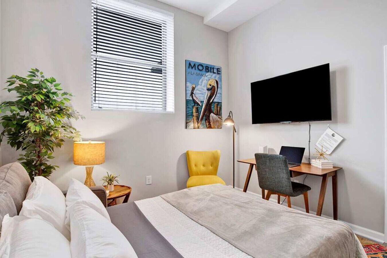 Ein modernes Hotelzimmer mit Bett, Schreibtisch, Sessel, Fernseher und einem Fenster mit Jalousien.