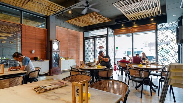 Un espace repas moderne avec des tables rondes, des chaises en osier et une grande fenêtre donnant sur la ville.