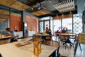 Un espace repas moderne avec des tables rondes, des chaises en osier et une grande fenêtre donnant sur la ville.