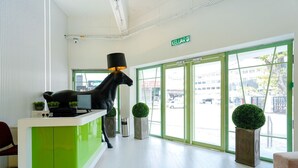 Un espace d’accueil moderne avec un comptoir vert et blanc, une statue de cheval noir et une vue sur la rue grâce à de grandes fenêtres.