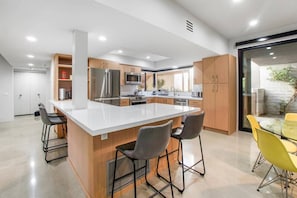 Una cocina moderna con una isla central, taburetes de bar y un comedor con sillas amarillas.