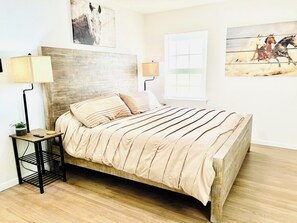 Une chambre à coucher avec une tête de lit en bois, un lit avec une literie à rayures, une table de chevet avec une lampe et des œuvres d’art accrochées aux murs.