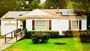 A single-story house with a front porch, a small garden, and solar panels on the roof. - Sports Themed 3-Bedroom Home in Arlington near AT & T Stadium & Other Sports  (Arlington)