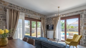 Ein modernes Wohnzimmer mit Steinwand, einem Holzesstisch, einem blauen Sofa, einem gelben Sessel und einem Fernseher an einer Steinwand.