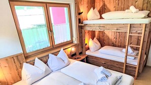 A wooden cabin room with bunk beds, a large bed, and a window with a view.