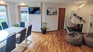 A modern interior with a wooden floor, a dining area with a table and chairs, a flat-screen TV mounted on the wall, and a seating area with bean bags.