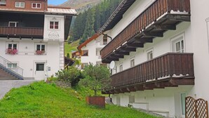 A traditional Alpine building with wooden balconies, a stone staircase, and a view of a mountain.