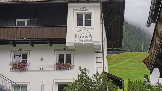 A building with a sign reading "FLANA APPAREMENTS" and a website address. It features multiple windows and balconies with flower boxes.