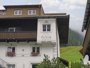 A building with a sign reading "FLANA APPAREMENTS" and a website address. It features multiple windows and balconies with flower boxes. - Typ III by Interhome (Mathon)