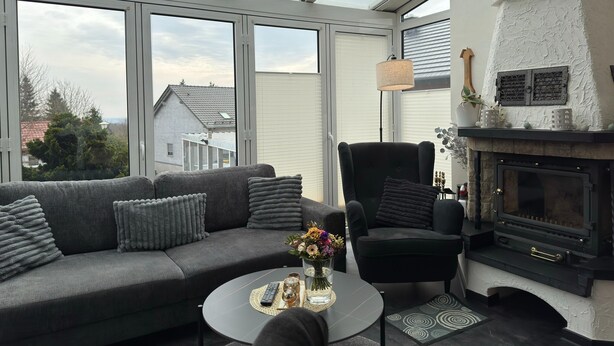 Ett modernt vardagsrum med en soffa, fåtölj, öppen spis och stora fönster.