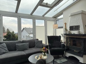 A modern living room with a sofa, armchair, fireplace, and large windows. - Ferienhaus mit Kamin in Thale-friedrichsbrunn (Thale)