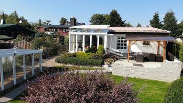 A residential property with a conservatory, a patio with outdoor furniture, and a garden with shrubs.