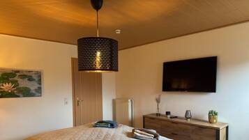 A bedroom with a bed, a dresser, a television, and a painting.