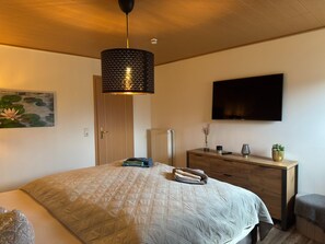 A bedroom with a bed, a dresser, a television, and a painting. - Ferienhaus mit Kamin in Thale-friedrichsbrunn (Thale)