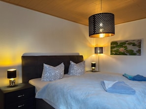 A bedroom with a bed, two bedside lamps, a nightstand, a wall-mounted lamp, and a painting of a lotus flower. - Ferienhaus mit Kamin in Thale-friedrichsbrunn (Thale)
