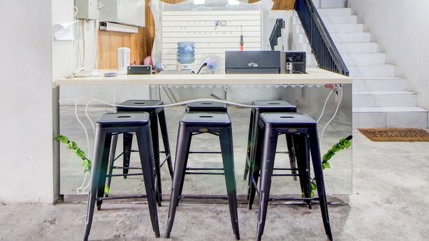 A workspace with a desk, three stools, a laptop, and a water dispenser. - Collection O Omah Joyo Solo Inn Near Keraton Surakarta (Surakarta)