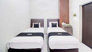 A hotel room with two single beds, a wooden panel wall, a small bedside table with a lamp, and a door. - Collection O Omah Joyo Solo Inn Near Keraton Surakarta (Surakarta)