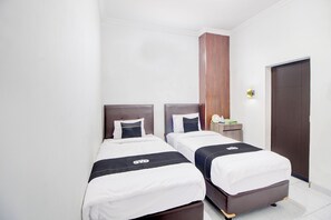 Habitación de hotel con dos camas, un armario de madera, una mesita de noche con lámpara y una puerta.
