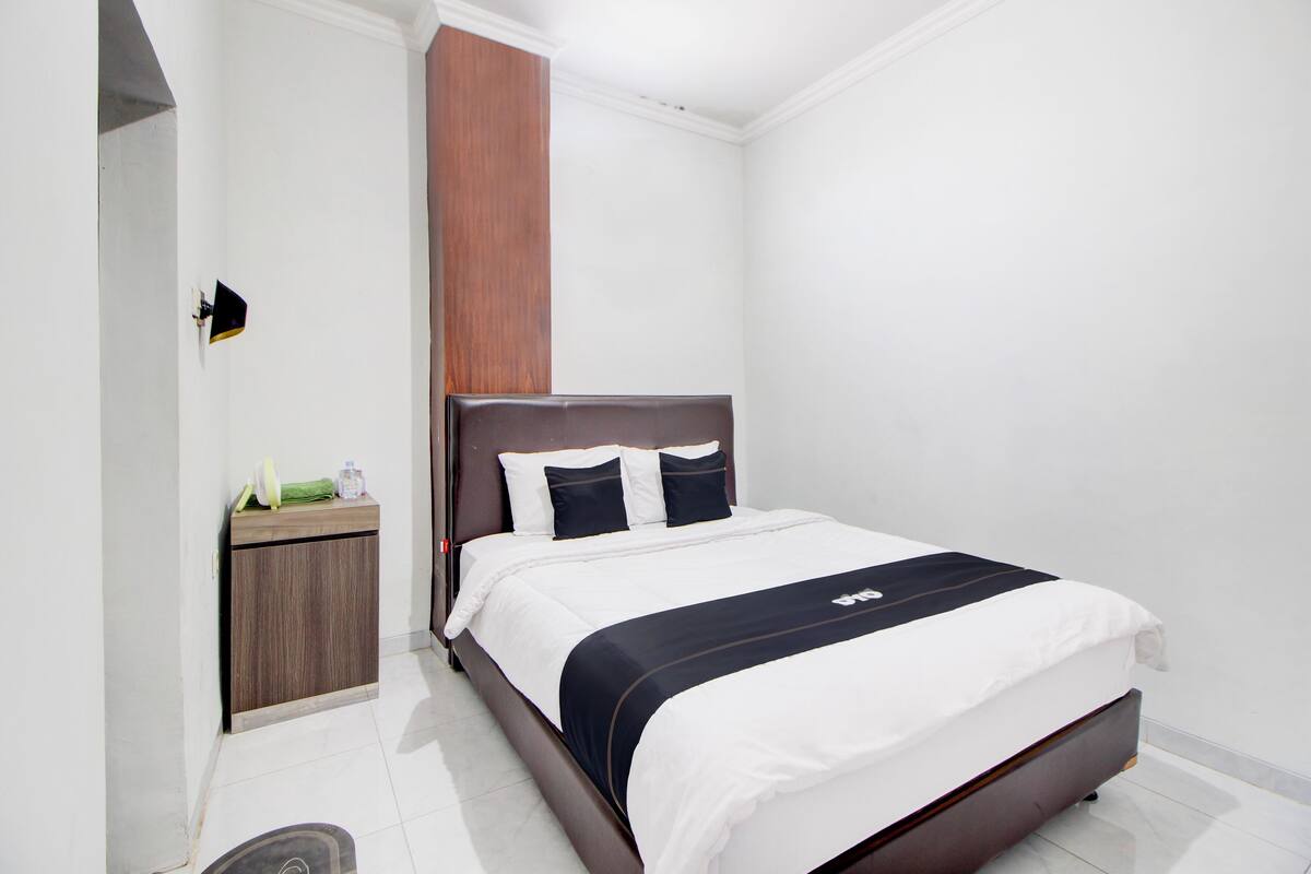 Una habitación de hotel moderna con una cama grande, cabecera de madera y una mesita de noche con lámpara.