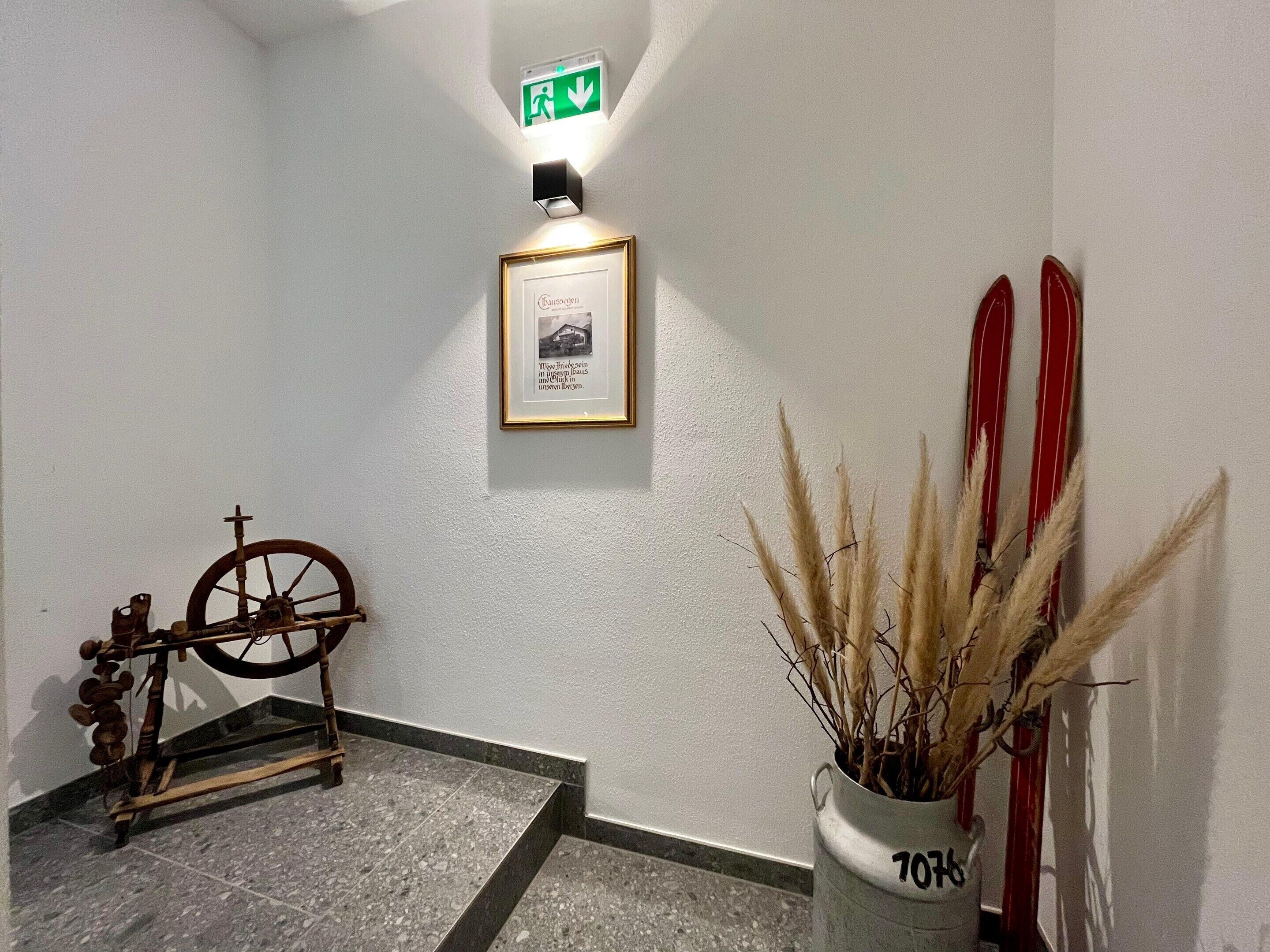 A hallway with a framed picture, a vintage bicycle, and a vase with dried plants.