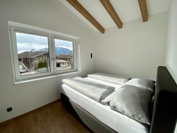 A bedroom with a bed, a window, and a view of buildings and mountains. - Attic Apartment Near Kitzsteinhorn Ski Area (Saalfelden am Steinernen Meer)