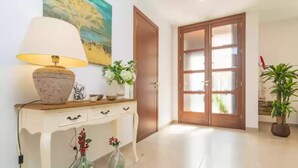 A hallway with a white console table, a lamp, and two vases with flowers. There is a wooden door and a glass door with frosted glass panels. - Villa Placeta - Villa With Private Pool. Free Wifi (, Illes Balears)