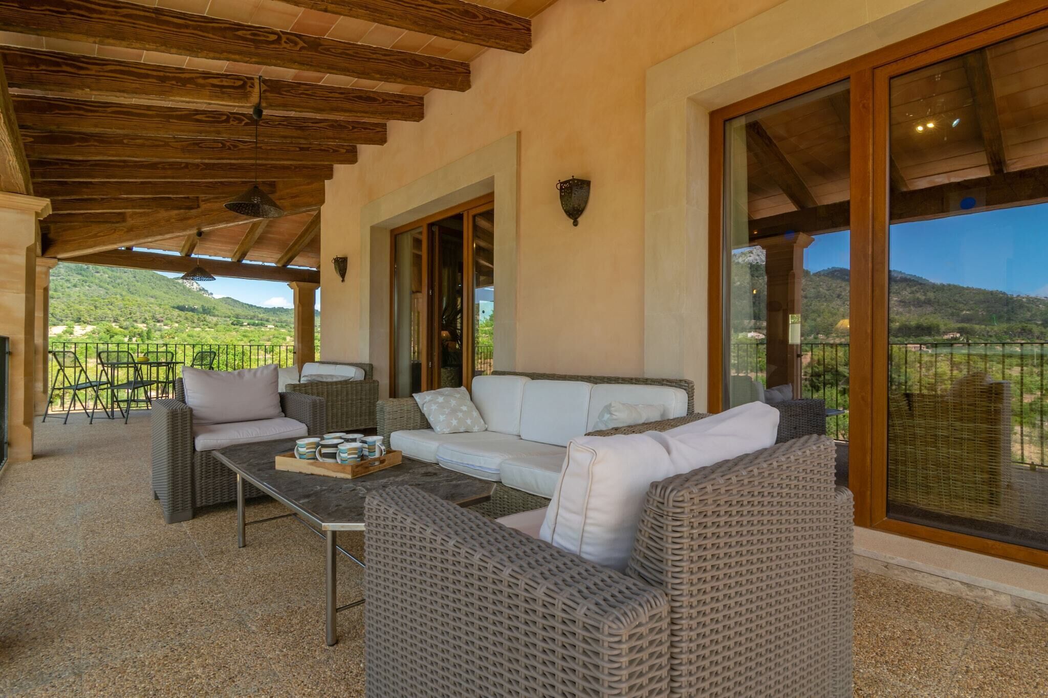 A covered outdoor seating area with wicker furniture, a table, and a view of a mountainous landscape.