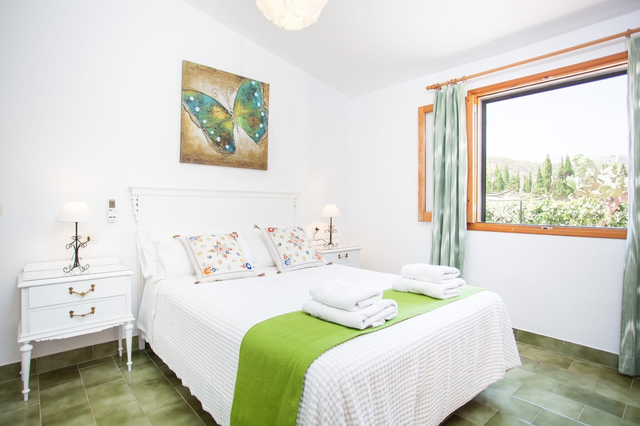 A bedroom with a bed, a nightstand, a lamp, a painting, and a window with curtains.