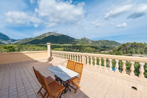 Une terrasse avec une table et des chaises, une balustrade et un paysage montagneux en arrière-plan.