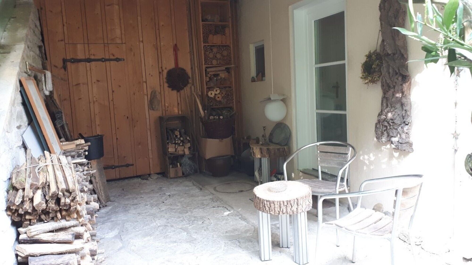A rustic wooden door, a metal chair, a small round table, and a plant.
