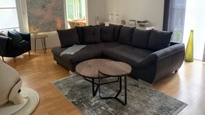 Una sala de estar moderna con un sofá seccional oscuro, una mesa redonda de centro y un cuadro abstracto grande en la pared.
