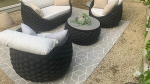 Un patio con dos sofás negros de ratán, una mesa redonda y una alfombra estampada.