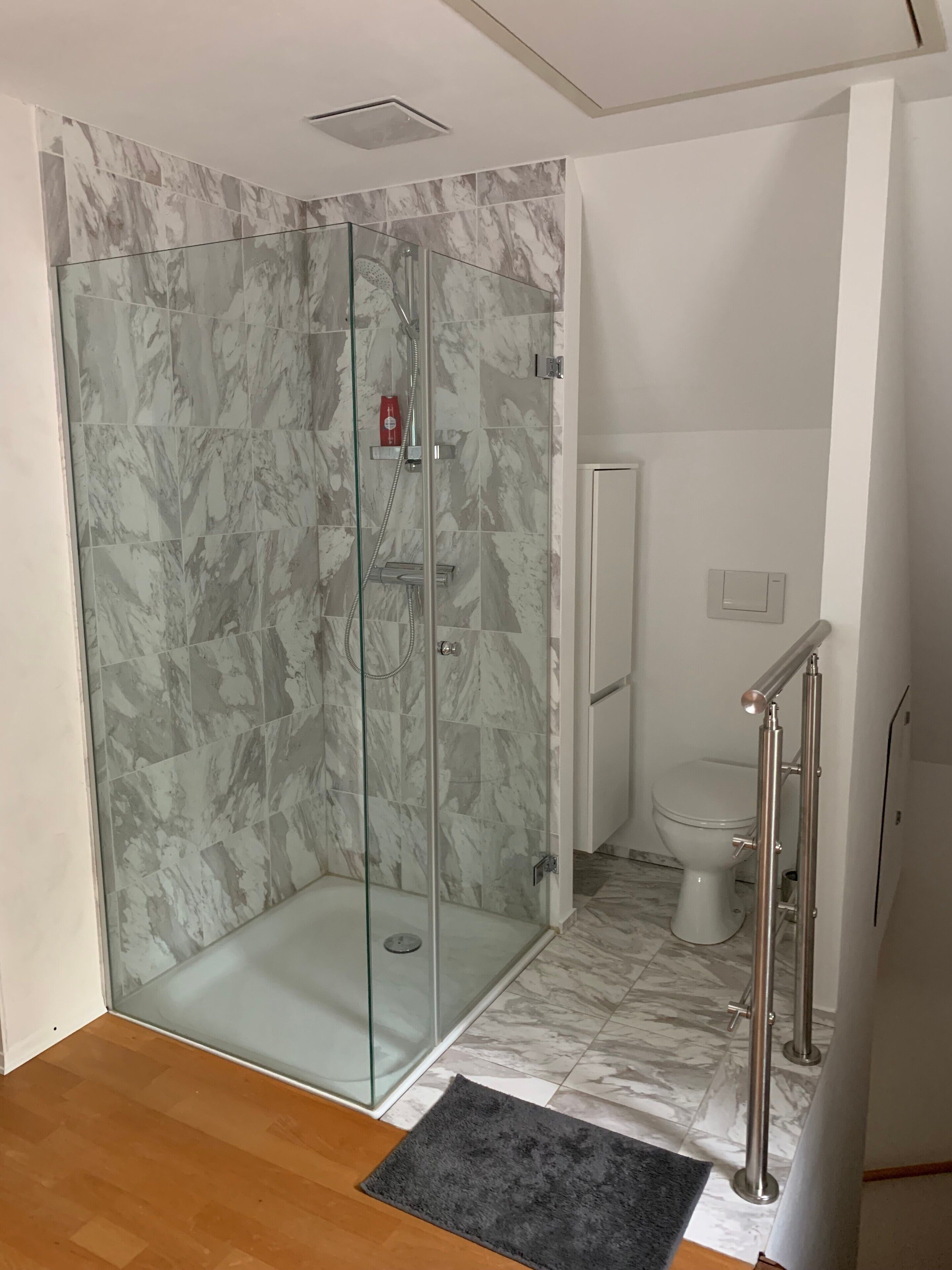 A bathroom with a glass-enclosed shower, a toilet, and a marble-tiled floor.