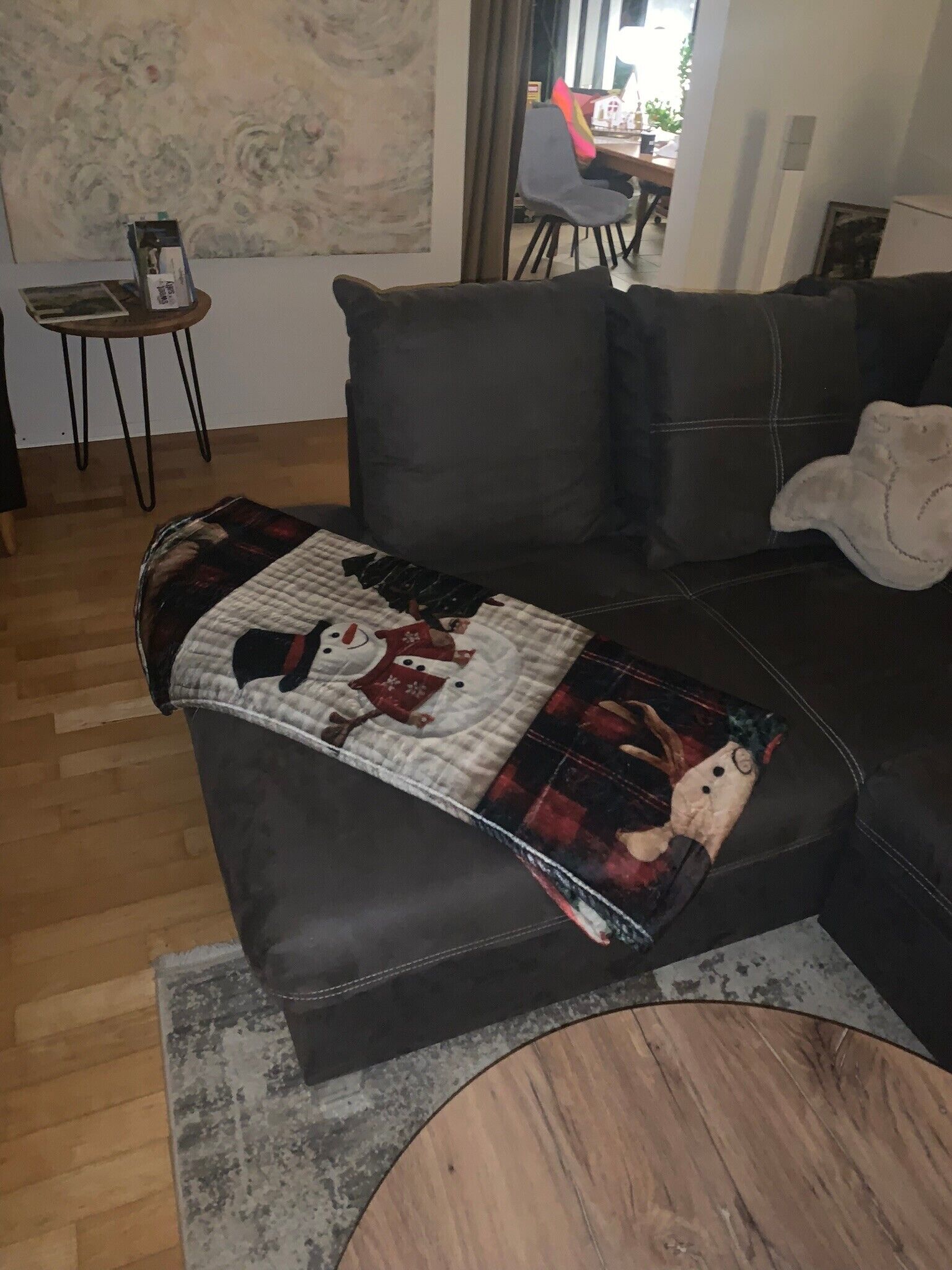 A living room with a dark leather sofa, a patterned throw blanket, a small wooden side table, and a chair.