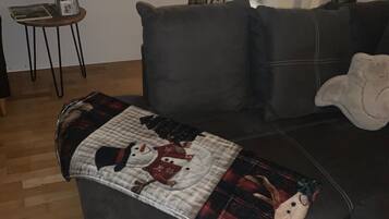 A living room with a dark leather sofa, a patterned throw blanket, a small wooden side table, and a chair.