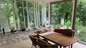 Un comedor con una mesa, sillas, un muro de piedra y vistas a zonas verdes a través de amplios ventanales.