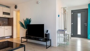 Uma sala de estar moderna com televisão de tela plana, mesa de centro, sofá, área de cozinha e uma porta.