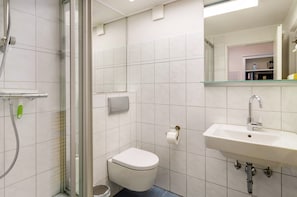 Un baño con cabina de ducha de vidrio, inodoro blanco, lavabo con espejo y pared con azulejos.