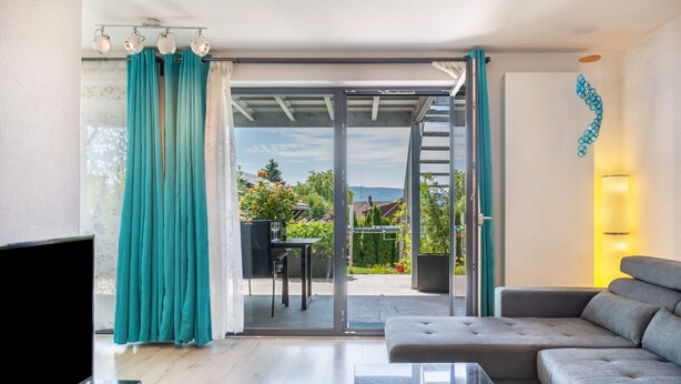 Uma sala de estar moderna com sofá, televisão e porta de vidro deslizante que dá para um pátio externo.