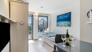 Ein modernes Zimmer mit einem Bett, einem Tisch mit Flasche und Gläsern, einem Gemälde und Blick durch eine Glastür.