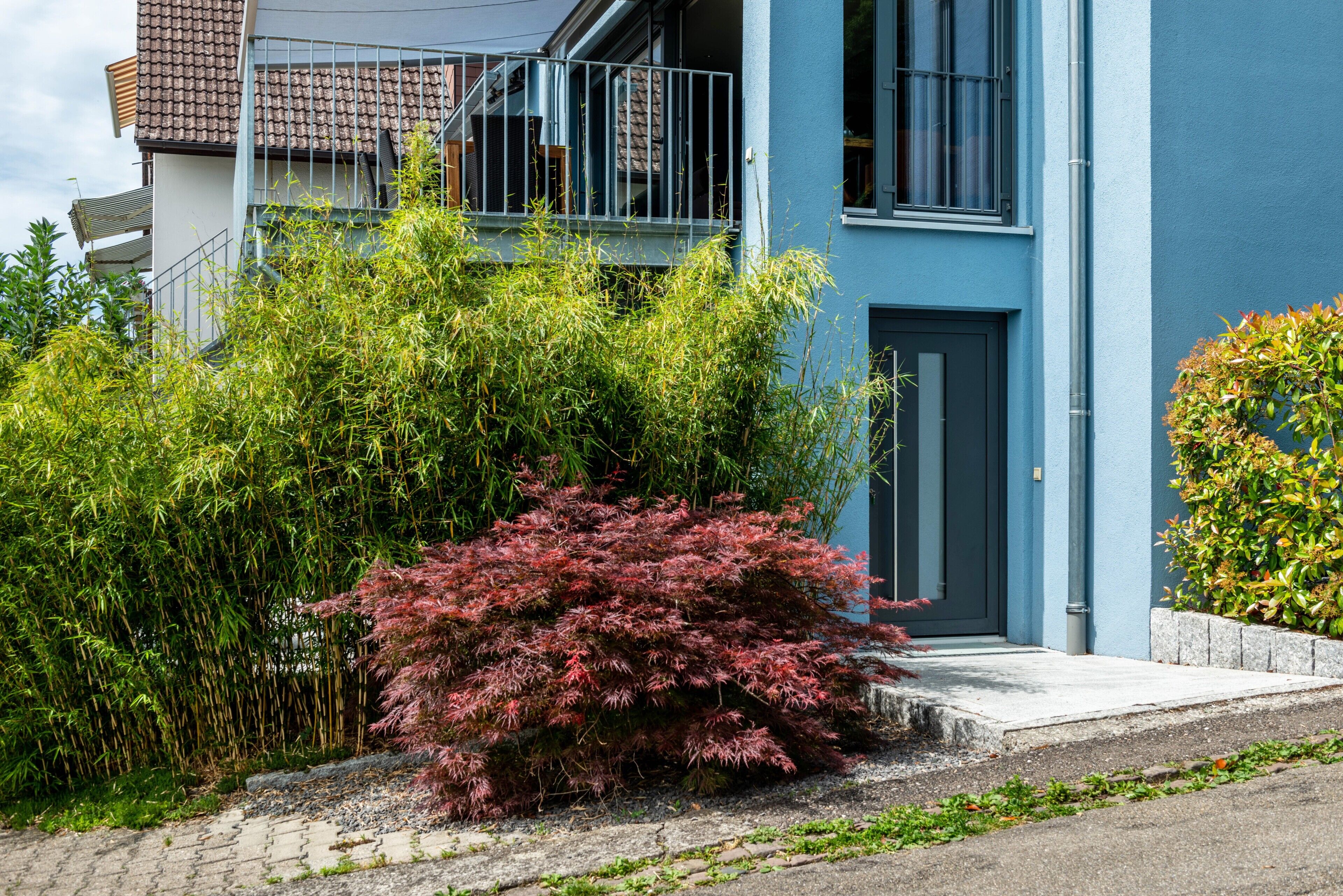 Een modern gebouw met twee verdiepingen, een blauwe gevel, een balkon en een goed onderhouden tuin met verschillende planten.